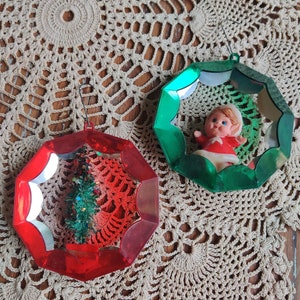 May include: Two vintage Christmas ornaments with a red and green reflective finish. One ornament features a small Christmas tree and the other features a small elf doll.