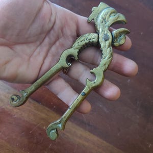 May include: A vintage brass nutcracker with a rooster head design. The nutcracker is a lever-style tool with a detailed, textured surface and a hinged mechanism. The rooster's head is at the top, and the handles have decorative curves.