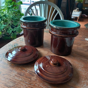 Puede incluir: Dos tarros de cerámica marrón con interiores turquesa y tapas a juego sobre una mesa de madera. Los tarros son cilíndricos con un diseño acanalado. Las tapas redondas tienen un pequeño pomo. Ideales para cocina o decoración del hogar.