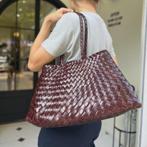 May include: A large, woven leather tote bag in a rich burgundy color. The bag features a braided handle and a spacious interior, perfect for carrying everyday essentials. The woven design adds a touch of texture and style.