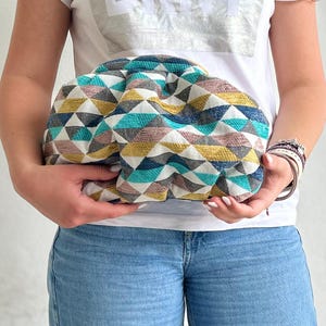 May include: A white, blue, gray, and gold geometric patterned clutch bag. The bag is puffy and has a rounded shape.