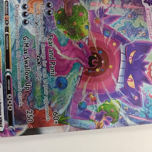 May include: A Gengar VMAX Pokemon card with a purple and pink background. The card features a Gengar VMAX Pokemon with a purple and black body and a pink and white face. The card has a single strike symbol and a HP of 320. The card also has a G-Max Swallow Up attack that does 250 damage and a Fear and Panic attack that does 60 damage for each of your opponent's Pokemon V and Pokemon GX in play.