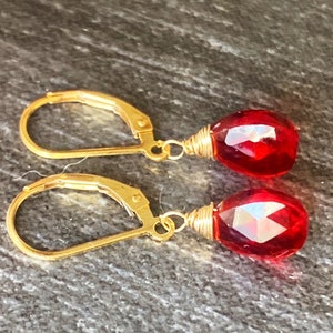 May include: A pair of gold earrings with red teardrop-shaped gemstone accents.