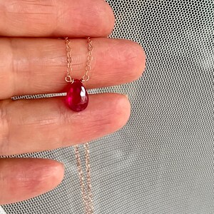 May include: A delicate gold chain necklace with a teardrop-shaped ruby pendant.