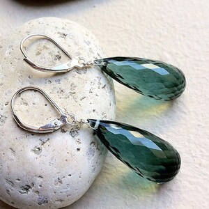 May include: A pair of silver dangle earrings with teardrop-shaped green gemstone pendants.