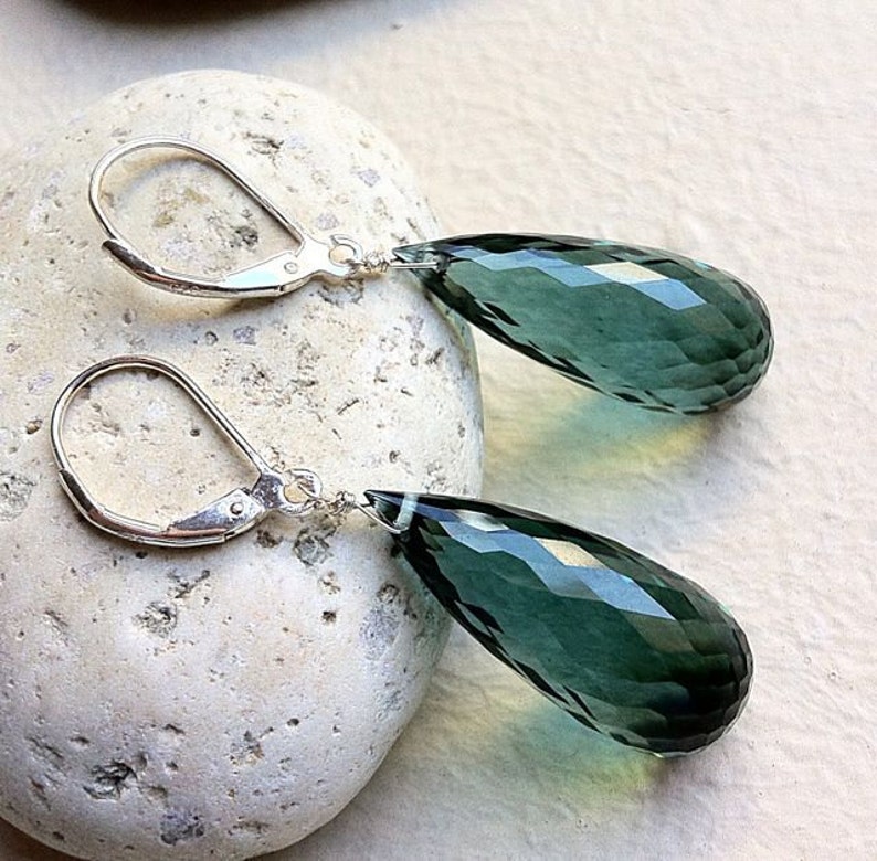 May include: A pair of silver dangle earrings with teardrop-shaped green gemstone pendants.