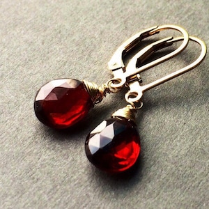 May include: A pair of gold earrings with red gemstone drops. The earrings have a simple wire design and are perfect for everyday wear.