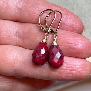 Pode incluir: Um par de brincos de ouro com gotas de pedras preciosas vermelhas em forma de lágrima.