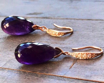 May include: A pair of dangle earrings with a teardrop-shaped amethyst gemstone and a rose gold setting. The earrings have a delicate design with small diamonds on the setting.