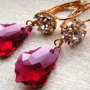 May include: A pair of gold dangle earrings with a teardrop-shaped red crystal and a cluster of clear rhinestones.
