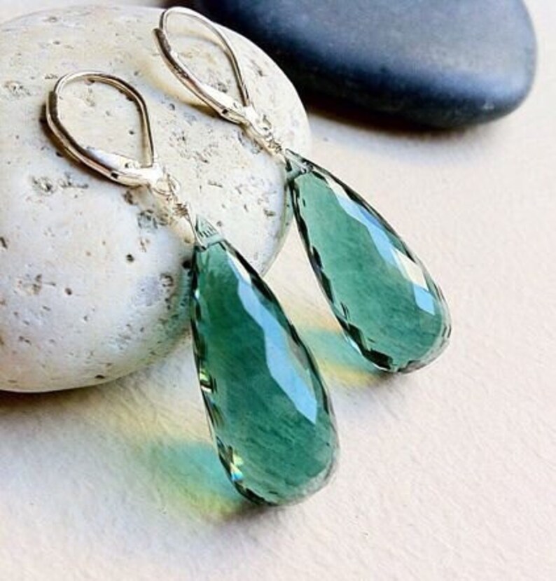 May include: A pair of silver dangle earrings with teardrop-shaped green gemstone pendants.