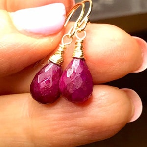 May include: A pair of gold wire wrapped earrings with ruby teardrop gemstones.