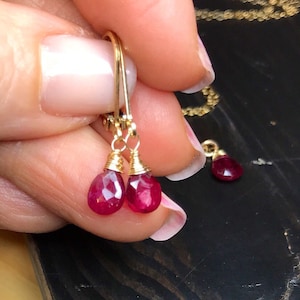 May include: Gold earrings with red gemstone teardrop dangles. The earrings are wire wrapped and have a simple design.