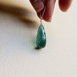 May include: A teardrop-shaped green gemstone earring with a silver wire loop.