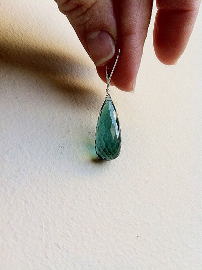 May include: A teardrop-shaped green gemstone earring with a silver wire loop.
