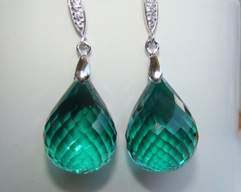 May include: A pair of silver dangle earrings with emerald green teardrop-shaped crystals. The crystals have a faceted design.
