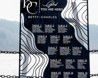 May include: Black and white wedding seating chart with a modern design. The chart features a white background with black lines and a black border. The text "We are so glad you are here!" is written in white cursive font. The names "Betty + Charles" are written in white font below the text. The chart is divided into 15 tables with guest names listed under each table number.