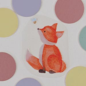 Könnte beinhalten: Ein skurriler Aufkleber mit einem Cartoon-Fuchs mit orangefarbenem und weißem Fell, der nach oben blickt. Der Fuchs ist von bunten, pastellfarbenen Kreisen umgeben. Der Aufkleber hat einen transparenten Hintergrund, und eine kleine Biene befindet sich über dem Fuchs.