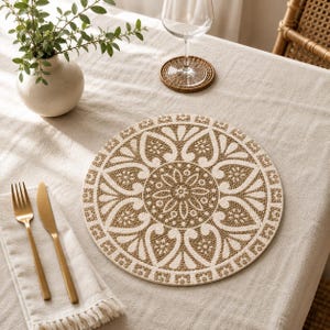 Peut inclure: Un set de table rond présentant une texture tissée avec un motif floral symétrique et répétitif en crème et beige. Le design se compose d'un motif circulaire central entouré de pétales stylisés et de bordures géométriques détaillées.