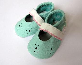 Könnte beinhalten: Ein Paar mintgrüne Babyschuhe mit Lochmuster. Die Schuhe haben weiße Riemen mit rosa gewellten Kanten. Die Innenseite der Schuhe ist dunkel türkis.