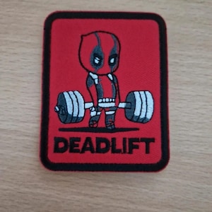 May include: A red, square patch with a black border, depicting a cartoon Deadpool character lifting a barbell. The word "DEADLIFT" is written in white block letters below the image.