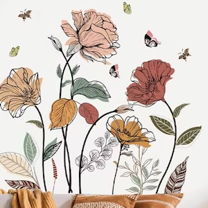 May include: Wall decal with a floral design. The decal features large, stylized flowers in peach, rust, and gold, outlined in black. Green and orange leaves and butterflies are scattered around the flowers. The background is white.