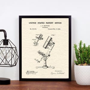 May include: A black and white vintage patent drawing of a microscope. The drawing is framed in a black frame and is on a wooden surface. The patent number is 513,703 and the patent date is March 13, 1903.