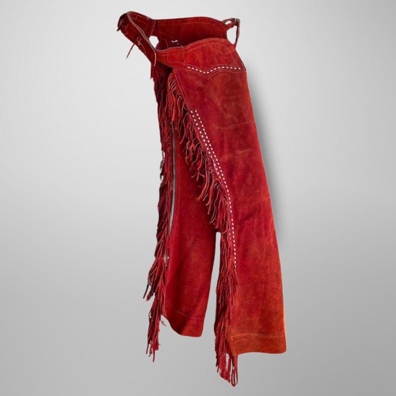 K&ouml;nnte beinhalten: Rote Wildleder-Chaps mit Fransen und wei&szlig;en N&auml;hten. Die Chaps haben einen Rei&szlig;verschluss vorne und eine G&uuml;rtelschlaufe oben.