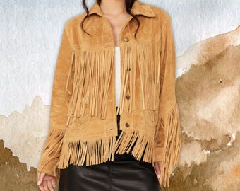 May include: A tan suede jacket with long fringe detailing on the chest, sleeves, and back. The jacket has a collared neckline and button closures. The jacket is paired with a black skirt. The overall style is Western-inspired.