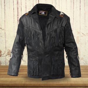 Könnte beinhalten: Schwarze Lederjacke mit Fransenbesatz und einem einzigen Knopfverschluss. Die Jacke hat ein gewebtes Design auf Vorder- und Rückseite sowie einen kleinen Patch auf der linken Brust.