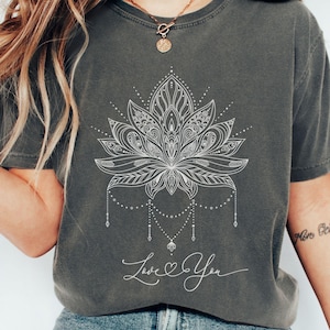 Pode incluir: Camiseta cinza com um desenho de flor de l&oacute;tus branca e a frase "Love You". A camiseta tem um corte folgado e mangas curtas. A cor da camiseta &eacute; "Pepper".
