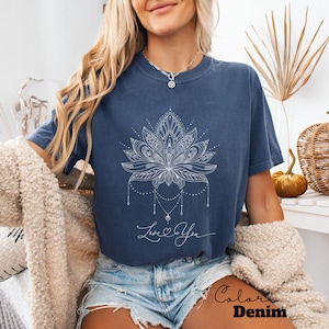 Pode incluir: Camiseta azul marinho com um desenho de flor de l&oacute;tus branca e as palavras "Love You" em escrita cursiva. A camisa est&aacute; rotulada como "Color Denim". A camiseta &eacute; de estilo casual.
