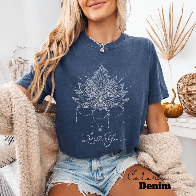 Pode incluir: Camiseta azul marinho com um desenho de flor de l&oacute;tus branca e as palavras "Love You" em escrita cursiva. A camisa est&aacute; rotulada como "Color Denim". A camiseta &eacute; de estilo casual.