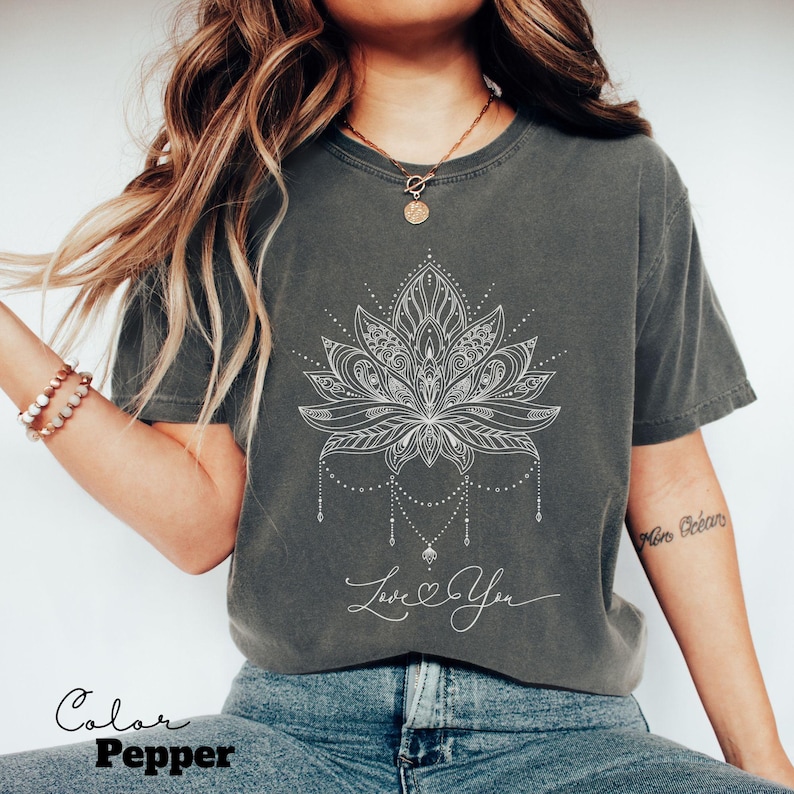 Pode incluir: Camiseta cinza com um desenho de flor de l&oacute;tus branca e a frase "Love You". A camiseta tem um corte folgado e mangas curtas. A cor da camiseta &eacute; "Pepper".