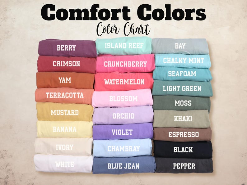Pode incluir: Um gr&aacute;fico de cores intitulado "Comfort Colors" exibe uma variedade de amostras de tecido dobradas. As cores incluem Berry, Crimson, Yam, Terracota, Mostarda, Banana, Marfim, Branco, Island Reef, Crunchberry, Watermelon, Blossom, Orchid, Violeta, Chambray e Blue Jean.