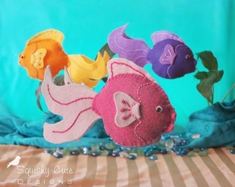 May include: Three felt fish toys in a rainbow of colors. The fish are pink, purple, and yellow with orange accents. The fish are sewn with white thread and have embroidered details.