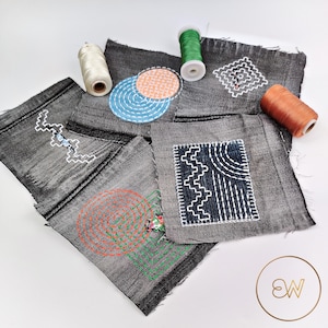 Può includere: Diversi campioni di tessuto denim grigio scuro con motivi ricamati a mano in bianco, blu, arancione e verde, tra cui cerchi, zig-zag e forme geometriche, accompagnati da tre rocchetti di filo bianco, verde e arancione.