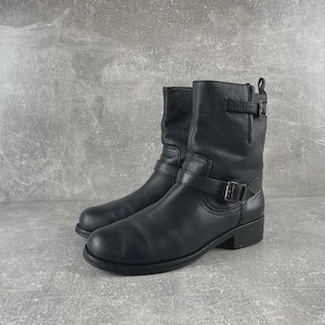 May include: A pair of black leather ankle boots. The boots have a rounded toe, a short heel, and a buckle strap around the ankle. The boots are made of a smooth, matte leather.