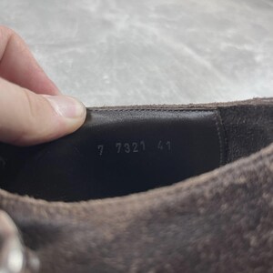 May include: Close-up of a brown suede shoe. The interior shows the numbers "7 7321 41" stamped in white. The shoe has a textured surface and a dark brown leather interior.