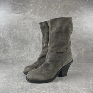 May include: A pair of gray suede boots with a mid-calf height. The boots have a rounded toe, a stacked heel, and a slouchy shaft. The heel height is approximately 3 inches.