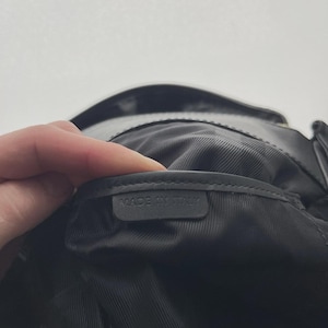 May include: Black leather bag interior with a textured lining. A label inside the bag reads "MADE IN ITALY". The bag is held open, revealing the inside.