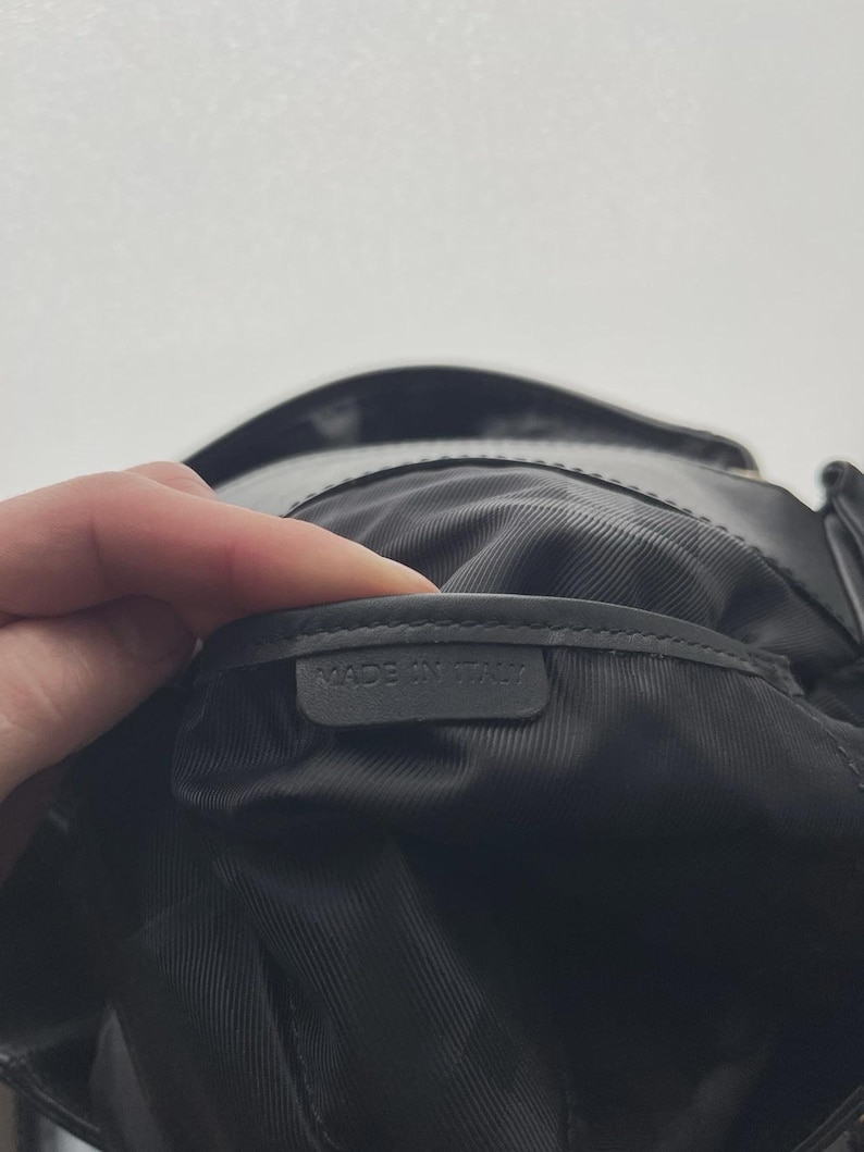 May include: Black leather bag interior with a textured lining. A label inside the bag reads "MADE IN ITALY". The bag is held open, revealing the inside.