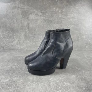 May include: A pair of dark blue leather ankle boots with a platform sole and high heels. The boots have a zipper closure and a rounded toe. The heels are approximately 4 inches high.