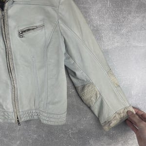 Peut inclure: Veste en cuir gris clair avec fermeture &eacute;clair et petite poche zipp&eacute;e sur la poitrine. La veste pr&eacute;sente des empi&egrave;cements &agrave; motifs peau de serpent sur les coudes et les poignets. La veste est pr&eacute;sent&eacute;e sur fond gris.
