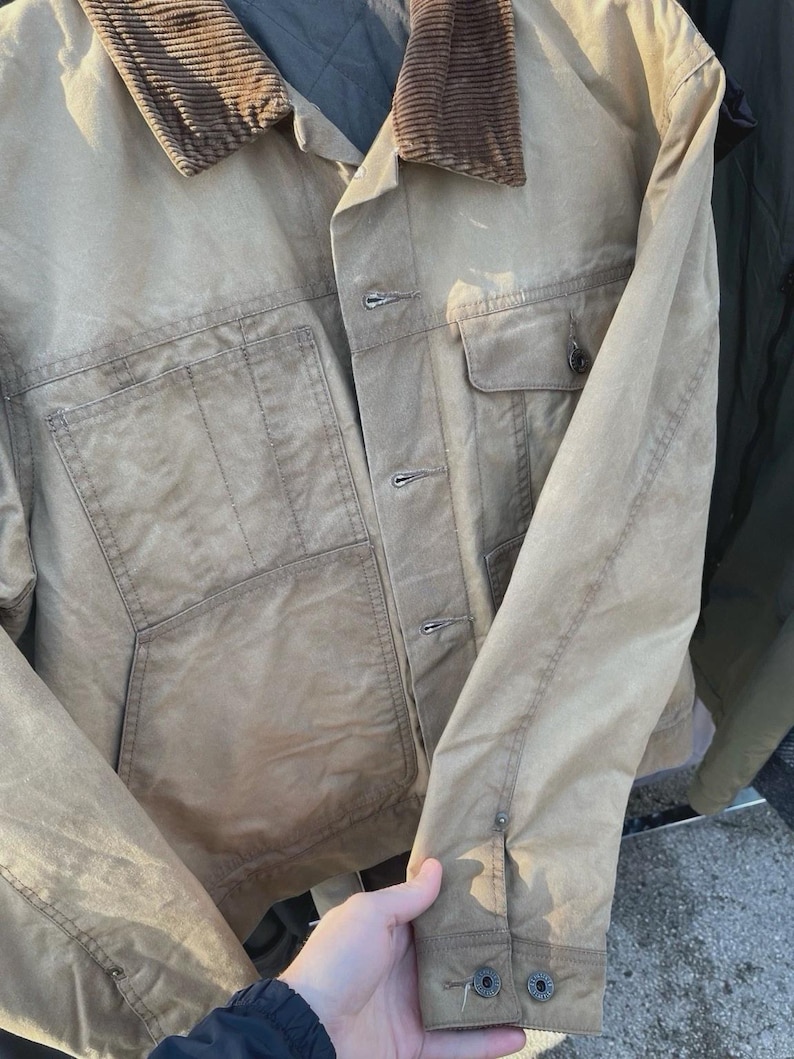 Puede incluir: Una chaqueta utilitaria de color tostado con cuello de pana marr&oacute;n, cierre frontal de botones y dos grandes bolsillos de parche. La prenda incluye un bolsillo en el pecho con solapa abotonada y mangas largas con pu&ntilde;os ajustables, con forro acolchado.