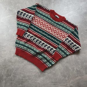May include: A red, green, and white patterned sweater. The sweater features a crew neck and ribbed cuffs and hem. The design includes diamond and geometric shapes.