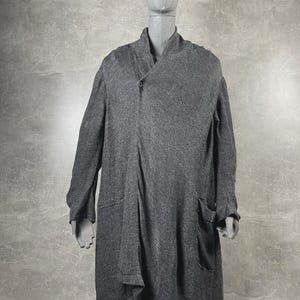 May include: A charcoal gray long-sleeve cardigan featuring an asymmetrical wrap-style front with a single button closure at the collar, long sleeves, and two large patch pockets on the lower front, displayed on a neutral-toned mannequin.