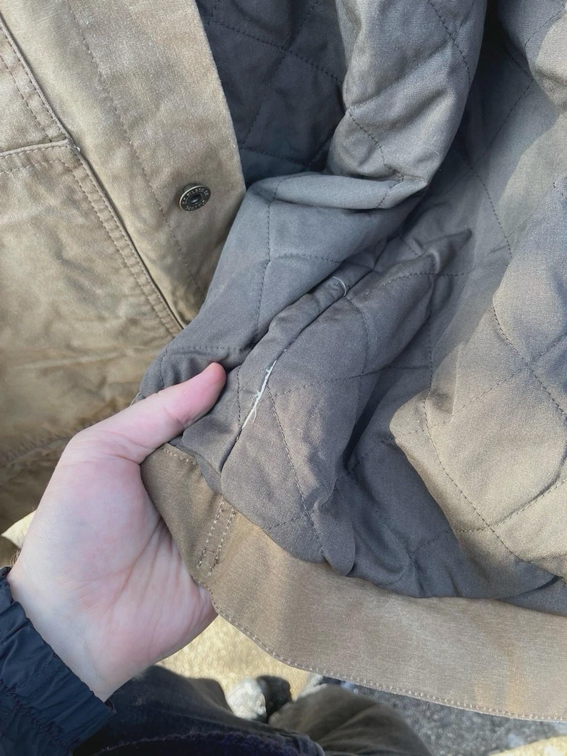 Puede incluir: Una chaqueta de color tostado con un forro acolchado gris oscuro. El exterior es de color tostado s&oacute;lido con un bot&oacute;n de presi&oacute;n met&aacute;lico visible. El interior presenta un patr&oacute;n de costuras en forma de diamante en tela gris oscuro.