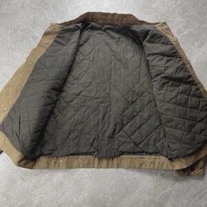 Puede incluir: Una chaqueta de color tostado con cuello de pana marr&oacute;n oscuro y forro acolchado gris oscuro. La chaqueta presenta una abertura frontal con botones de presi&oacute;n met&aacute;licos a lo largo de la tapeta y los pu&ntilde;os, con costuras visibles.