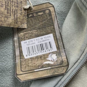 May include: A light green hoodie with a zip closure, viewed close up. A tag is attached, showing the text "AMERICAN MADE FOREVER", product details, and a barcode. The hoodie is made of 100% cotton.